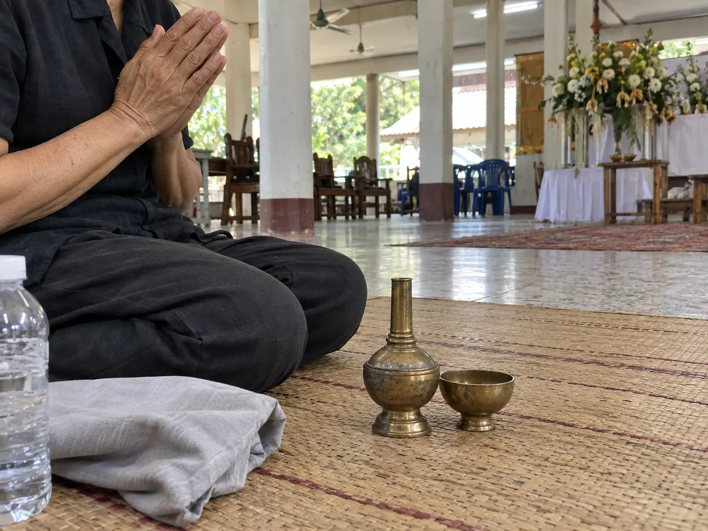 ที่กรวดน้ำทองเหลืองวางบนเสื่อข้างมือที่พนมอยู่ ในศาลาวัดไทย