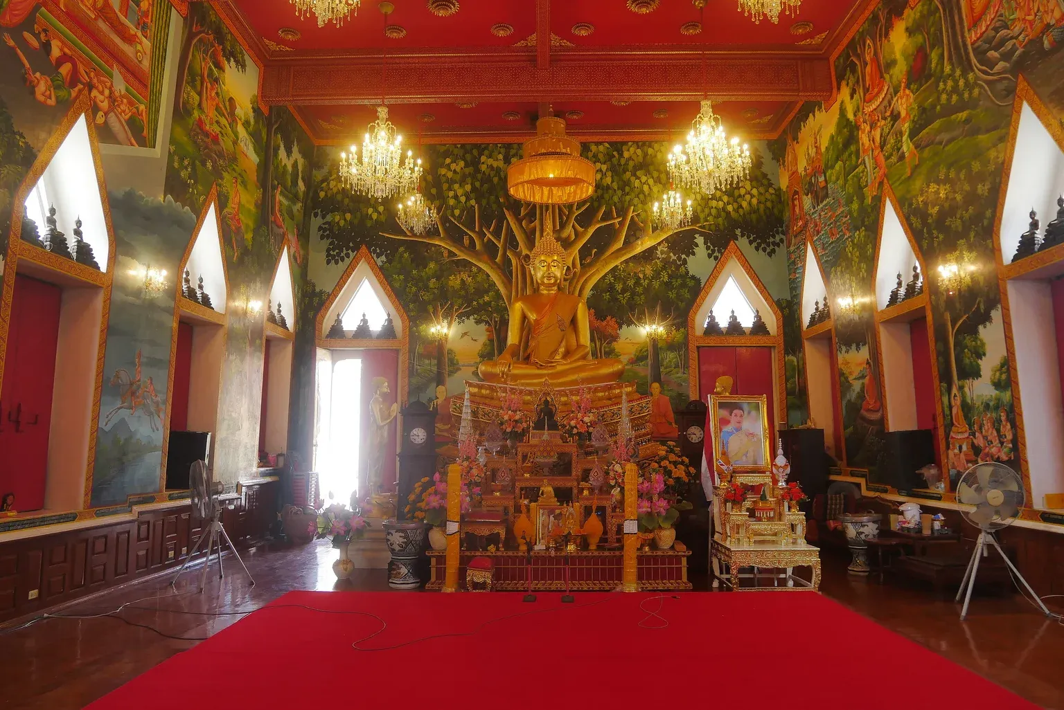พระประธานสีทองปางมารวิชัยหน้าภาพเขียนต้นโพธิ์ ภายในอาคารวัดบึงทองหลาง ผนังเขียนภาพพุทธประวัติ พื้นไม้ปูพรมแดง