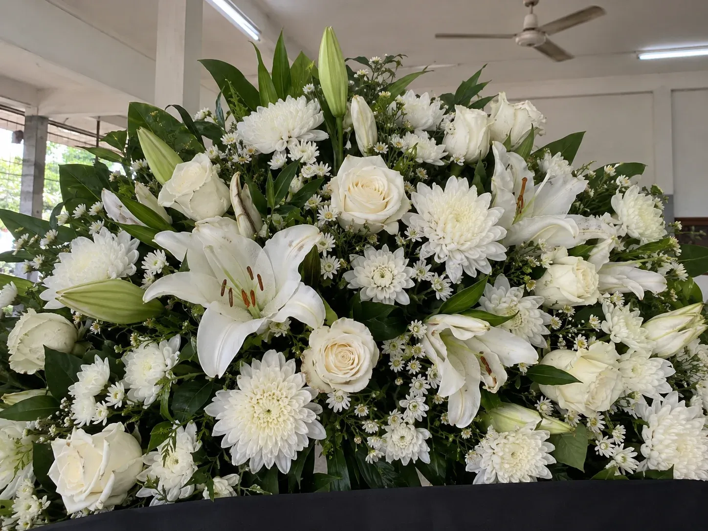 พวงหรีดดอกไม้สดโทนขาวเขียว ดอกลิลลี่ กุหลาบ และเบญจมาศเรียงแน่น ถ่ายใกล้