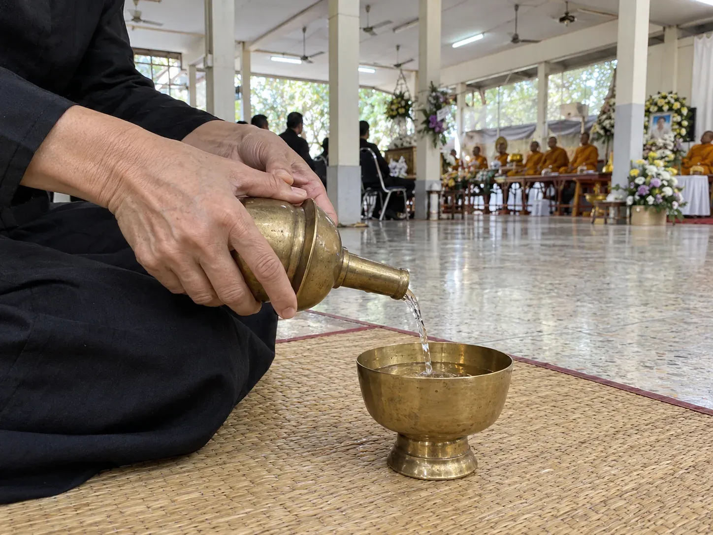 มือรินน้ำจากที่กรวดน้ำทองเหลืองลงขันใบเล็ก ระหว่างพระสงฆ์ให้พรในศาลาวัด