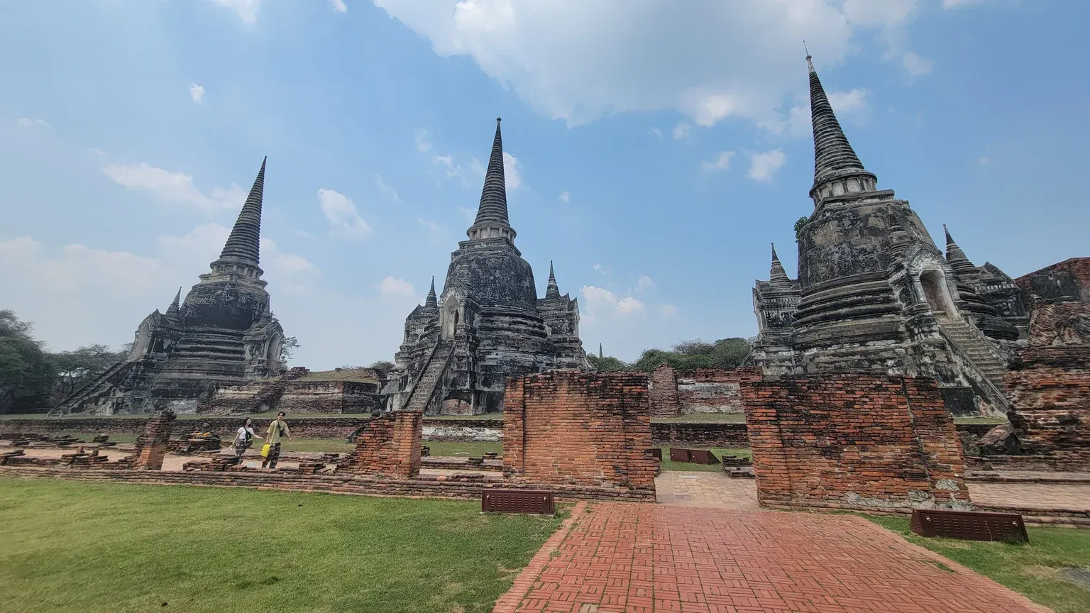 เจดีย์สามองค์วัดพระศรีสรรเพชญ์มุมกว้าง แต่ละองค์มีมุขและบันไดทางขึ้น ด้านหน้าเป็นผนังอิฐเตี้ยและทางเดินอิฐ ท้องฟ้าสีฟ้า