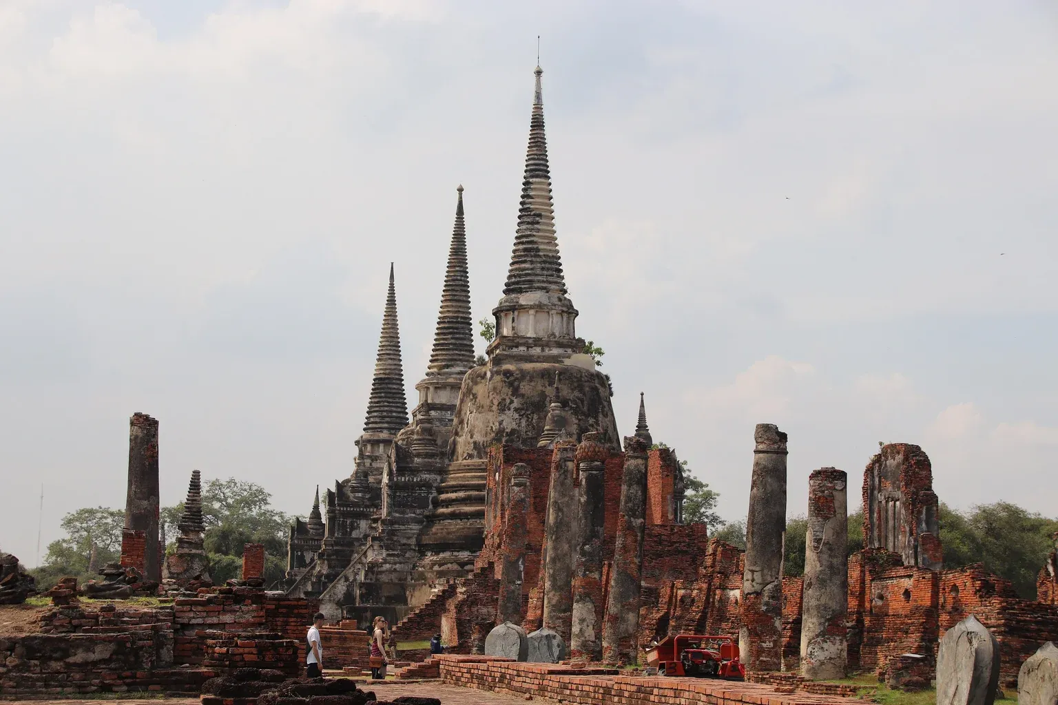 เสาและผนังอิฐของซากวิหารวัดพระศรีสรรเพชญ์ ด้านหลังเห็นยอดเจดีย์สามองค์เรียงซ้อนกัน