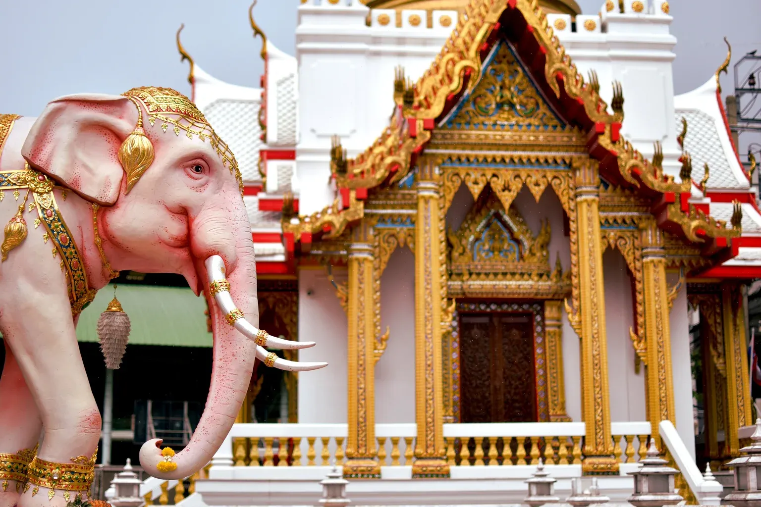 รูปปั้นช้างสีชมพูทรงเครื่องสีทอง หน้าอาคารสีขาวหน้าบันสีทองในวัดเสมียนนารี