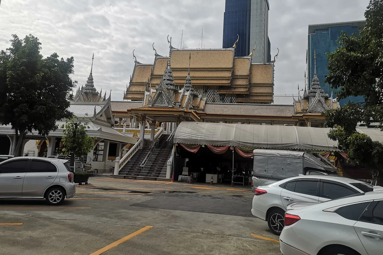 อาคารหลังคาซ้อนชั้นกระเบื้องสีทองของวัดศรีเอี่ยม มีบันไดขึ้นชั้นบน ด้านหน้าเป็นเต็นท์ผ้าใบและลานจอดรถ