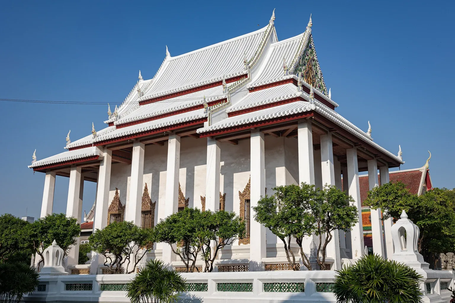 พระอุโบสถวัดโสมนัสราชวรวิหาร เสาสี่เหลี่ยมสีขาวรอบอาคาร หลังคาซ้อนชั้นสีขาวขอบแดง ซุ้มหน้าต่างสีทอง