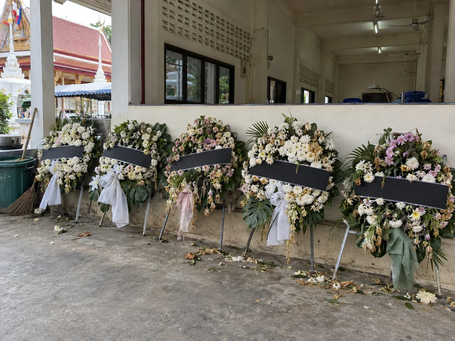 พวงหรีดดอกไม้สดที่ดอกเริ่มเหี่ยว ตั้งเรียงริมผนังด้านนอกศาลาวัดหลังจบงาน